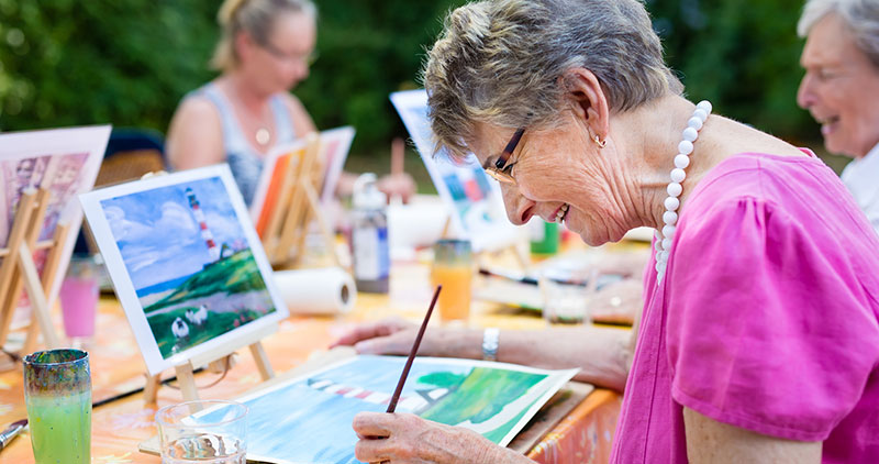 Smiling senior woman painting with group